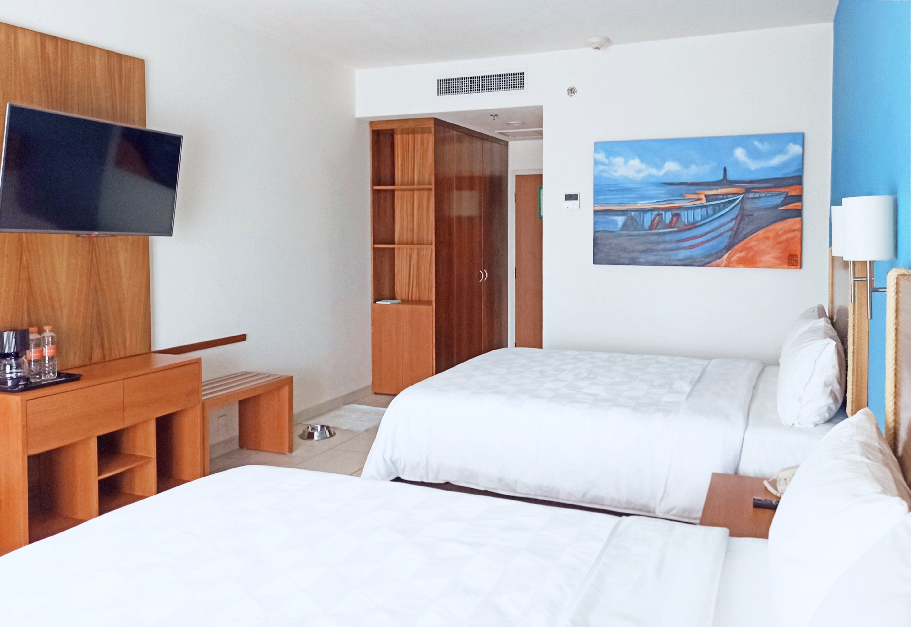 Une chambre d’hôtel avec deux lits, une télévision, un bureau avec une chaise et un tableau au mur.