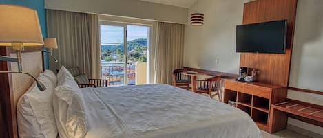 A hotel room with a bed, a desk, a television, and a view of a resort.