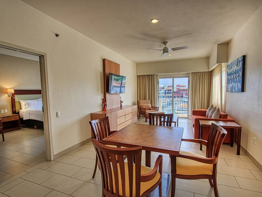 A hotel room with a dining area, a bed, a TV, and a balcony with a city view.
