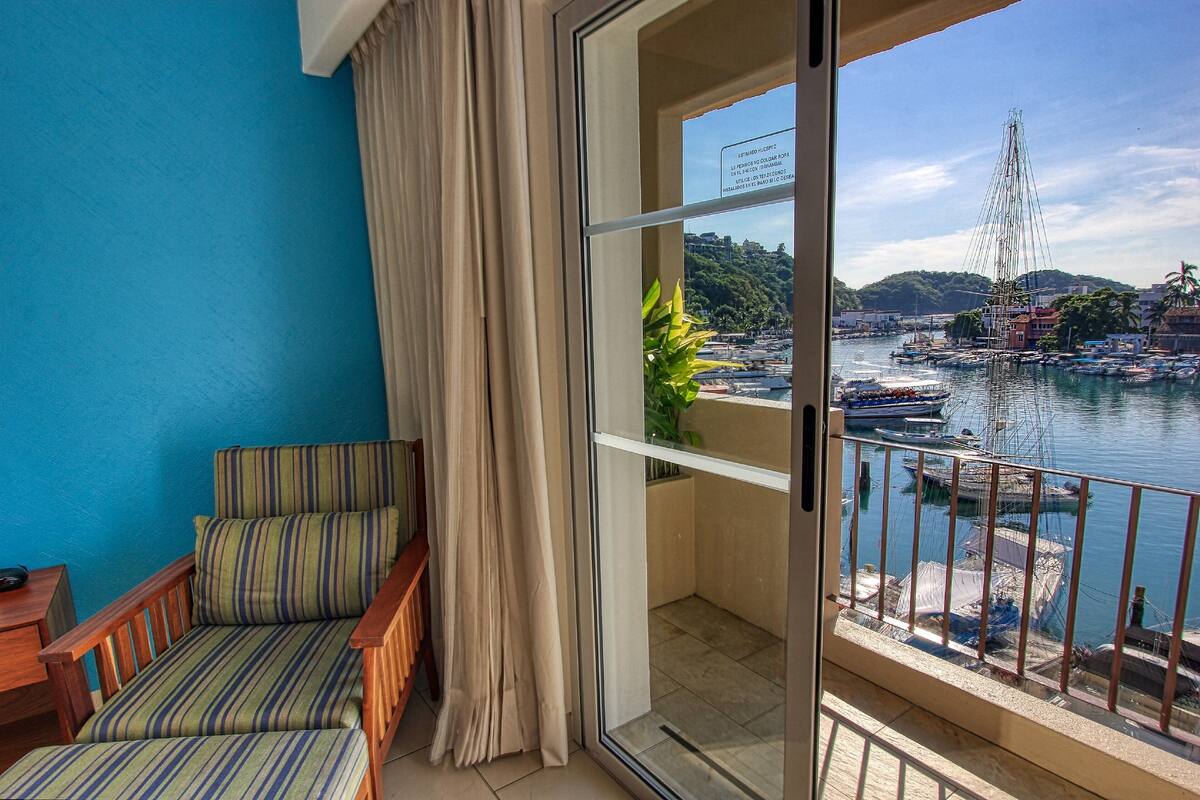 A balcony with a view of a harbor, a chair, and a plant.
