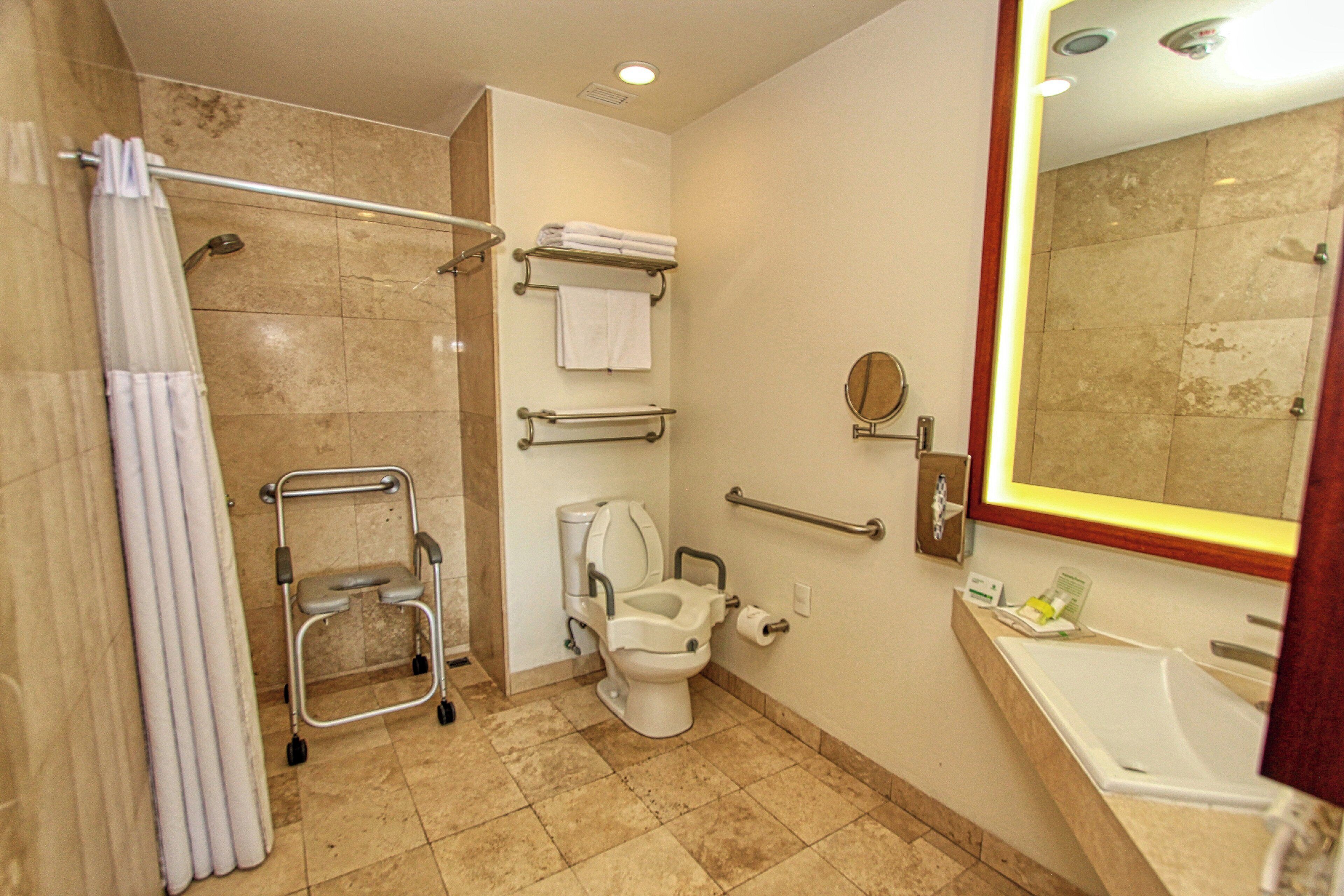 Un baño con ducha, inodoro, barra de apoyo y lavamanos.