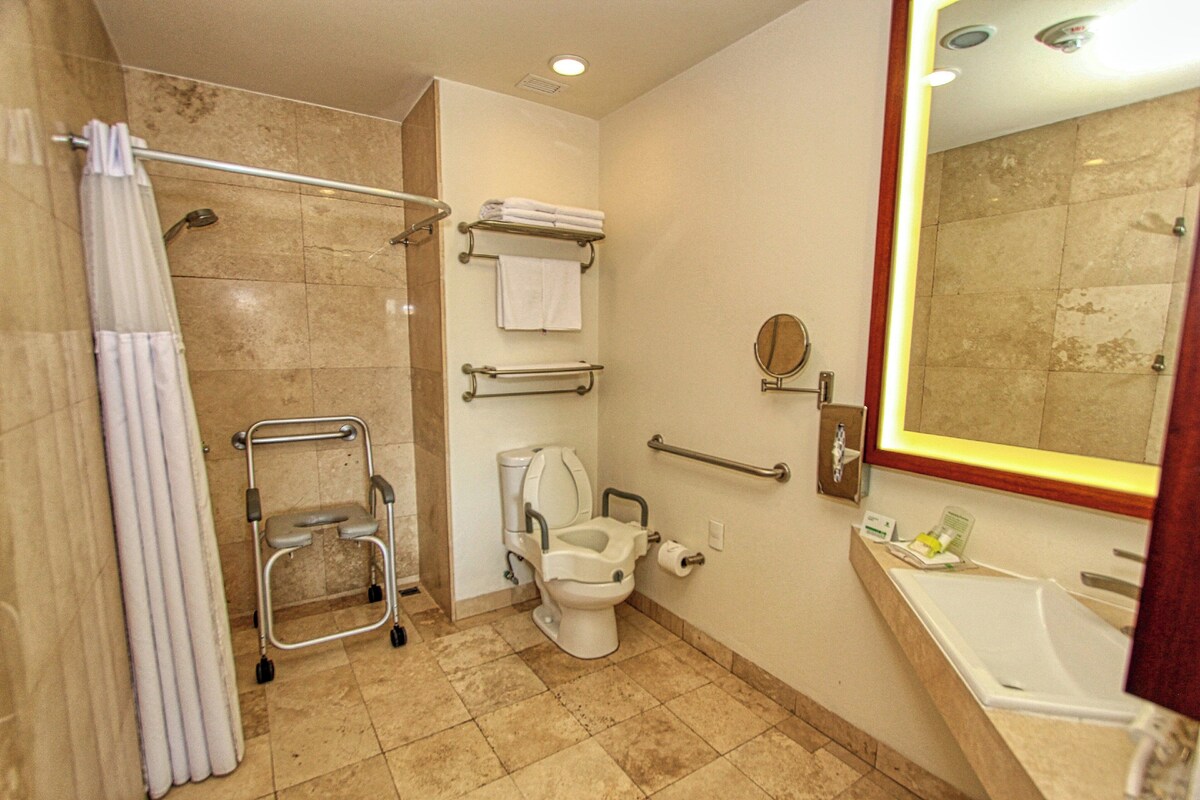 A bathroom with a shower, toilet, grab bar, and a sink.