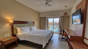 Une chambre d’hôtel avec un lit, un bureau, une chaise, une télévision et un balcon avec vue.