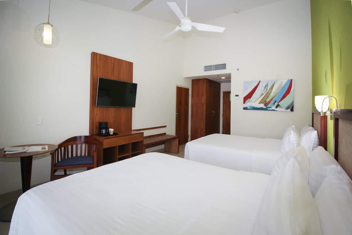 A hotel room with two beds, a desk with a chair, a television, and a painting on the wall.