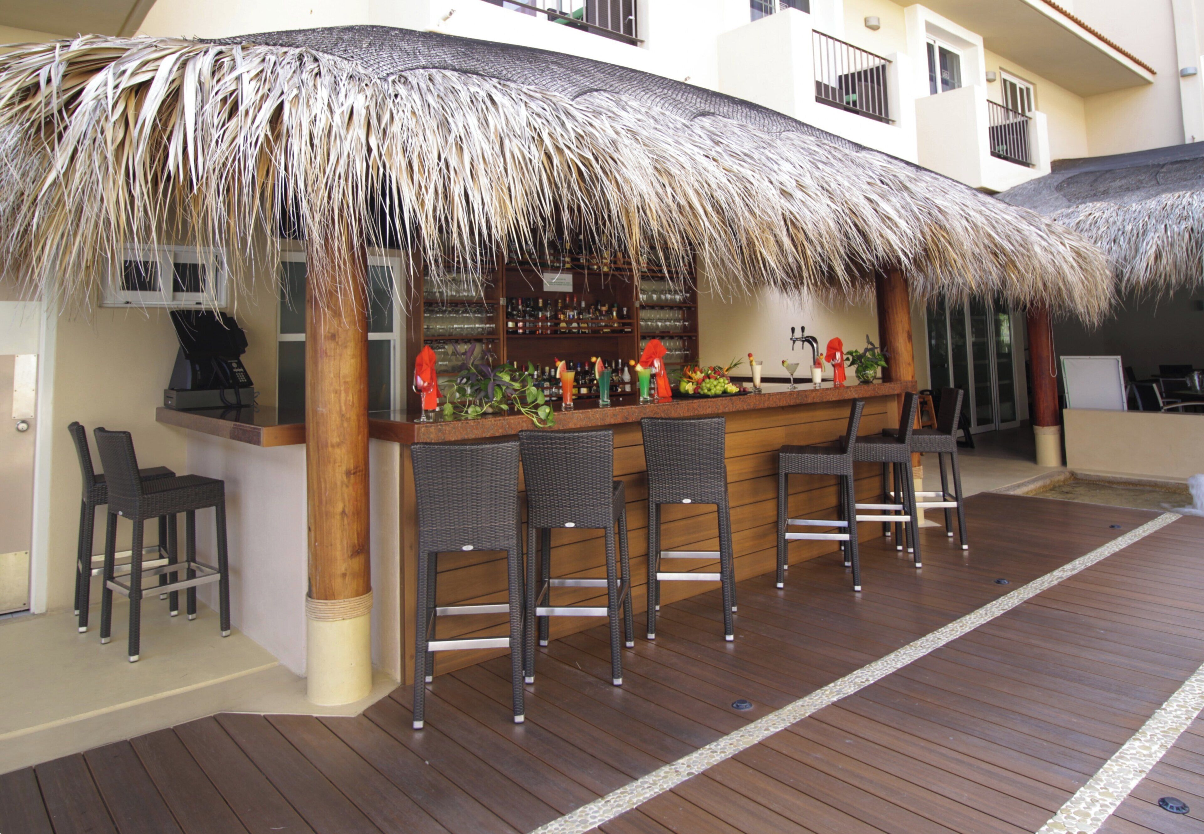 Zona de bar con techo de paja, mostrador de madera y sillas de mimbre.