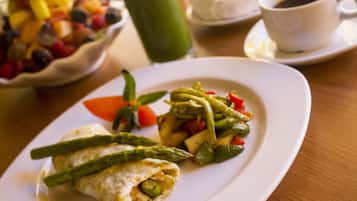 A plate with a wrap containing vegetables, a cup of coffee, and a bowl of fruit salad on a table.