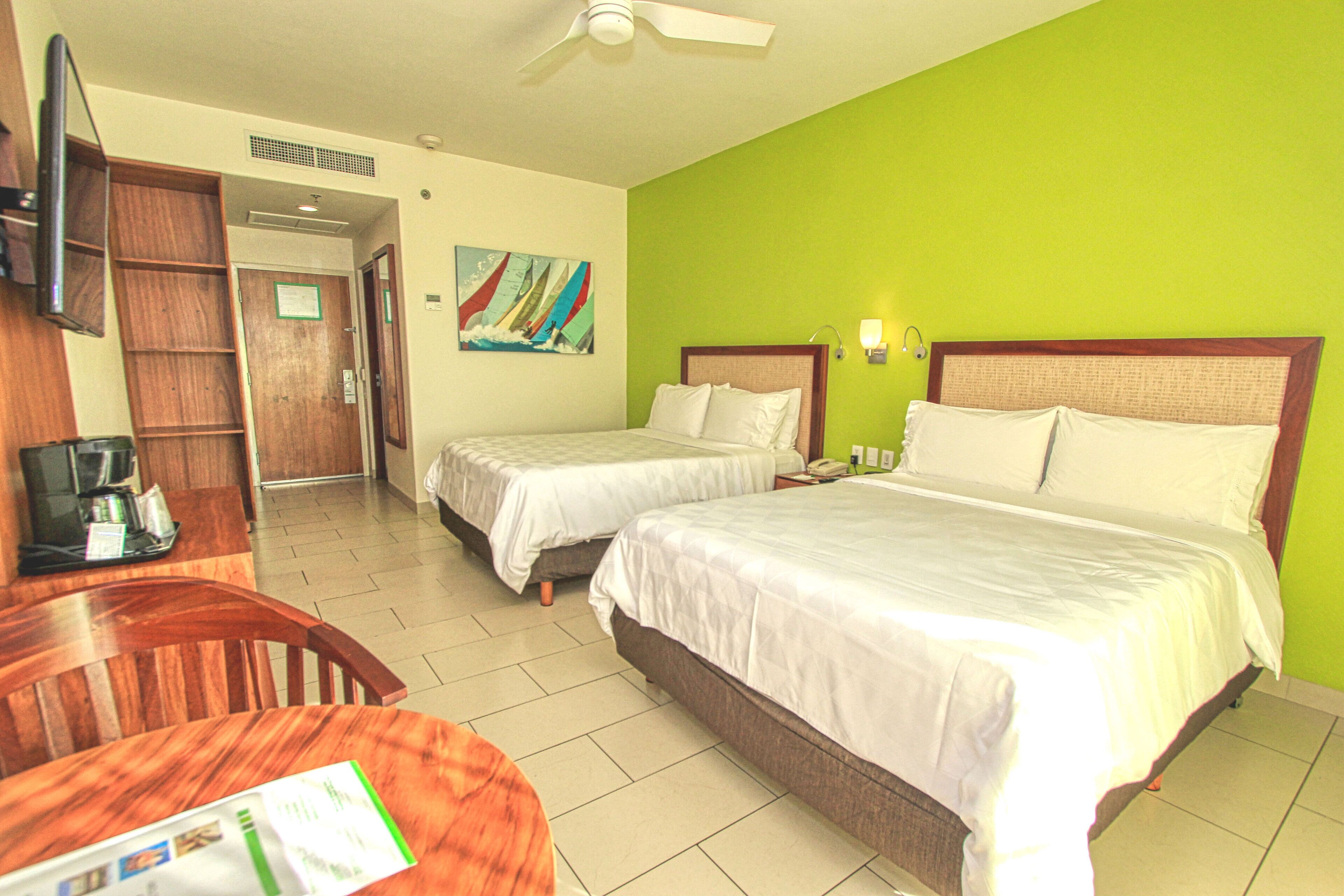 A hotel room with two beds, a desk with a chair, a television, and a painting on the wall.