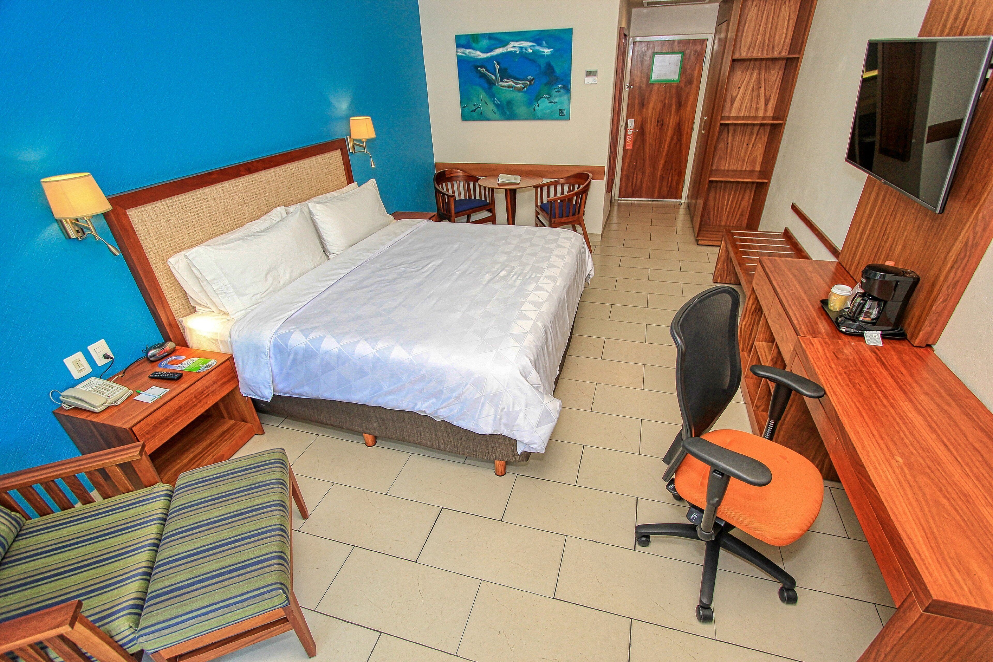 Une chambre d’hôtel avec un lit, un bureau, une chaise, une télévision et un tableau au mur.