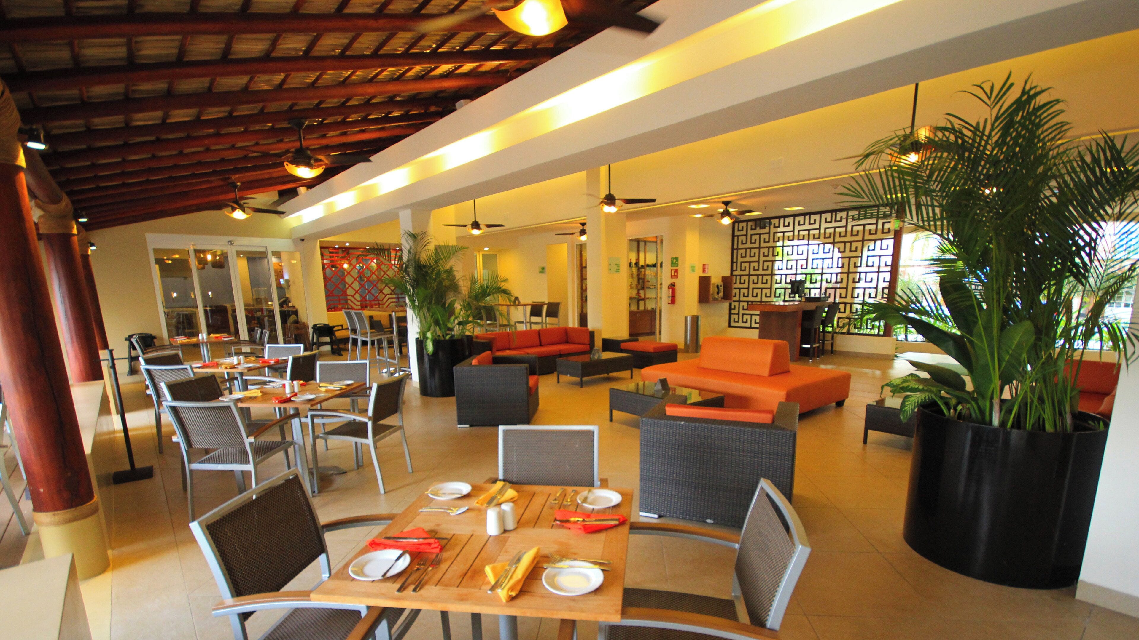 A hotel lobby with seating areas, tables set for dining, and potted plants.
