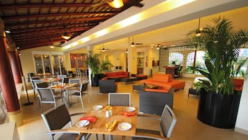 A hotel lobby with seating areas, tables set for dining, and potted plants.