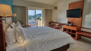Une chambre d’hôtel avec un grand lit, un bureau avec une chaise, un téléviseur fixé au mur et une vue sur l’extérieur.