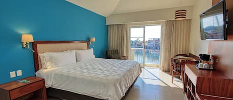 Habitación de hotel con una cama grande, un escritorio con silla, televisión y un balcón con vistas.