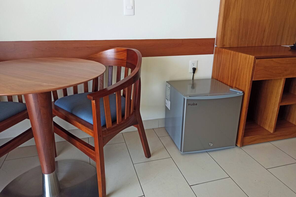 A compact room with a wooden dining table and chairs, a small refrigerator, and a wooden cabinet.