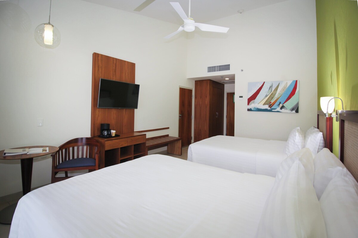 A hotel room with two beds, a desk with a chair, a television, and a painting on the wall.