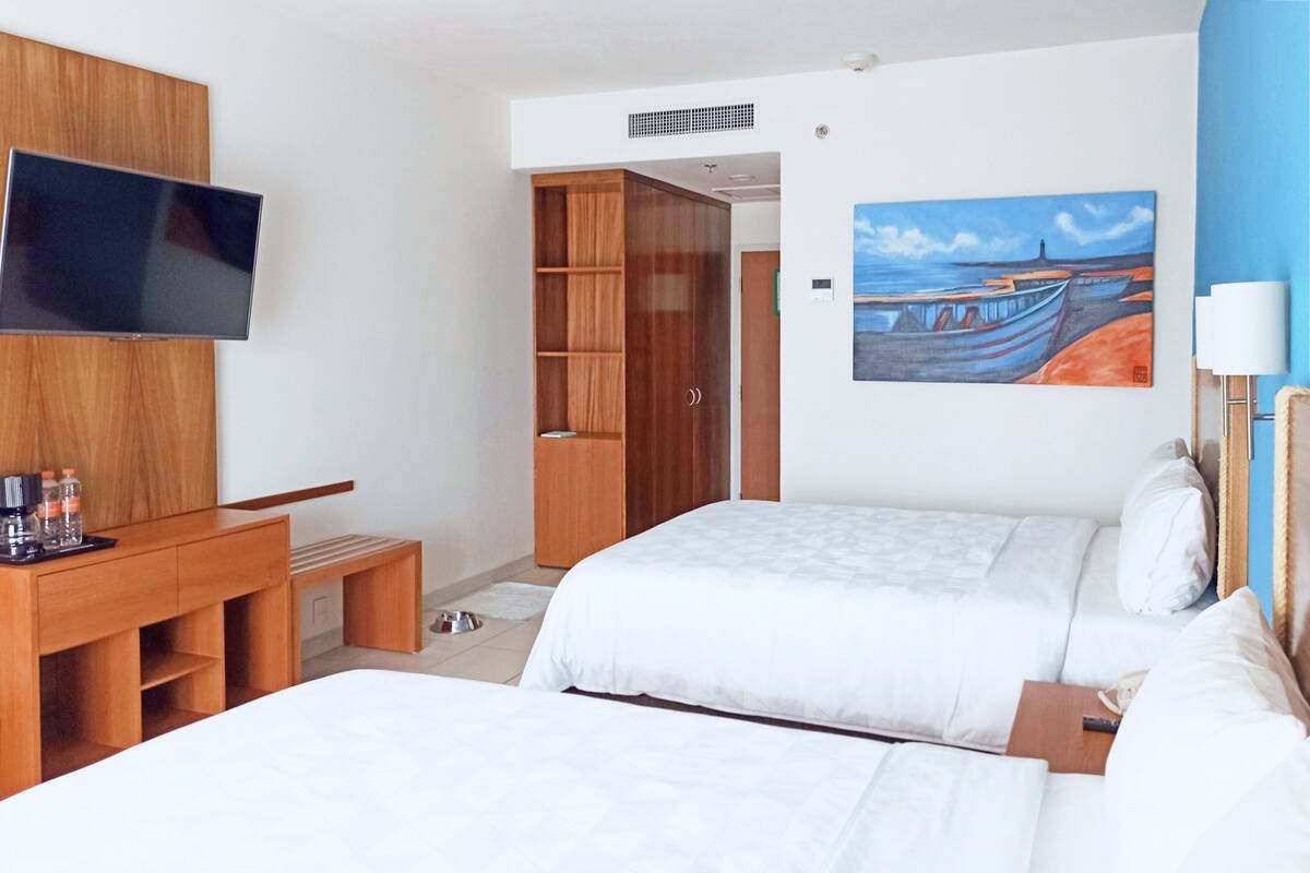 A hotel room with two beds, a TV, a wooden wardrobe, a desk with a chair, and a painting on the wall.