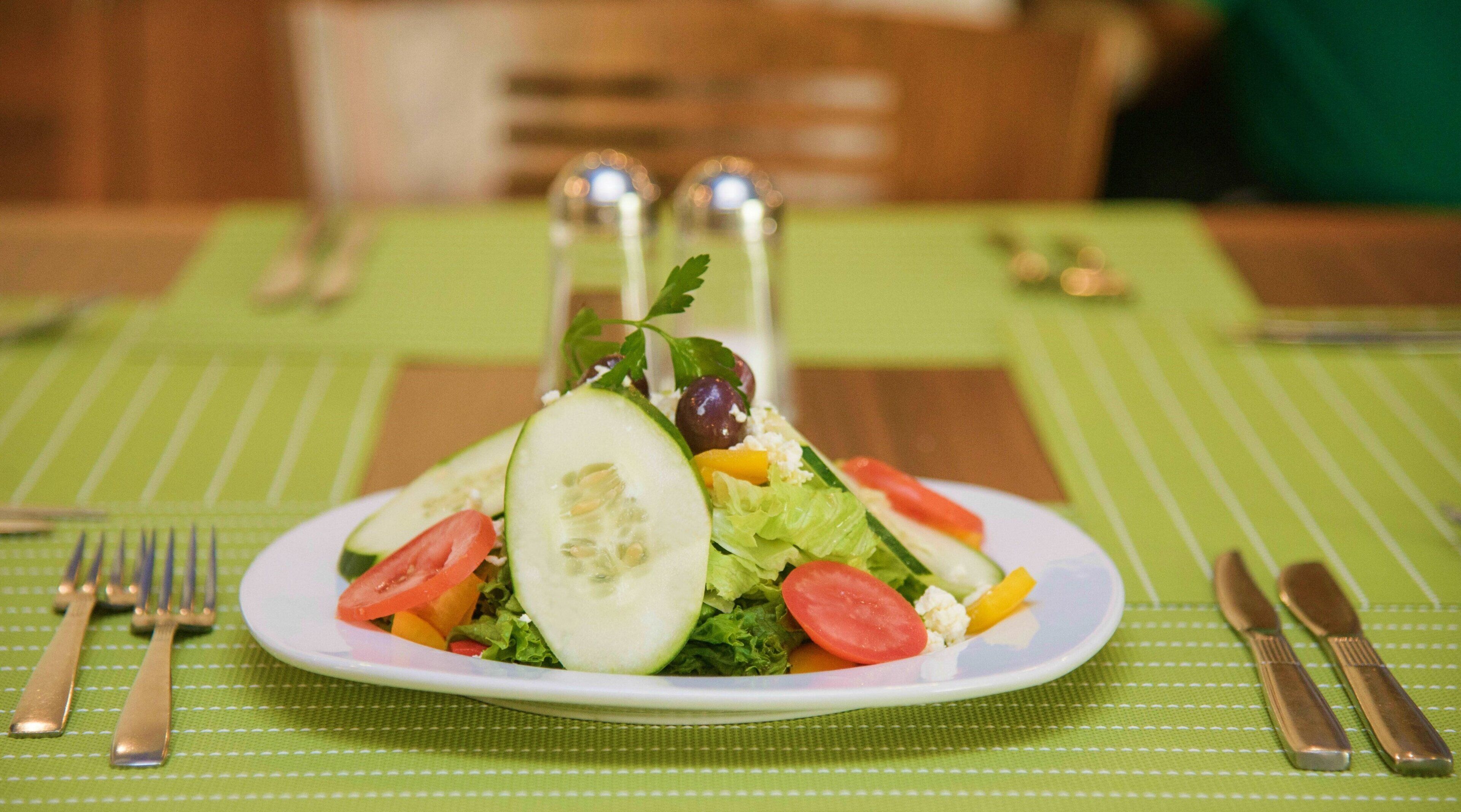 A plate of salad on a green tablecloth with a fork and knife to the left.