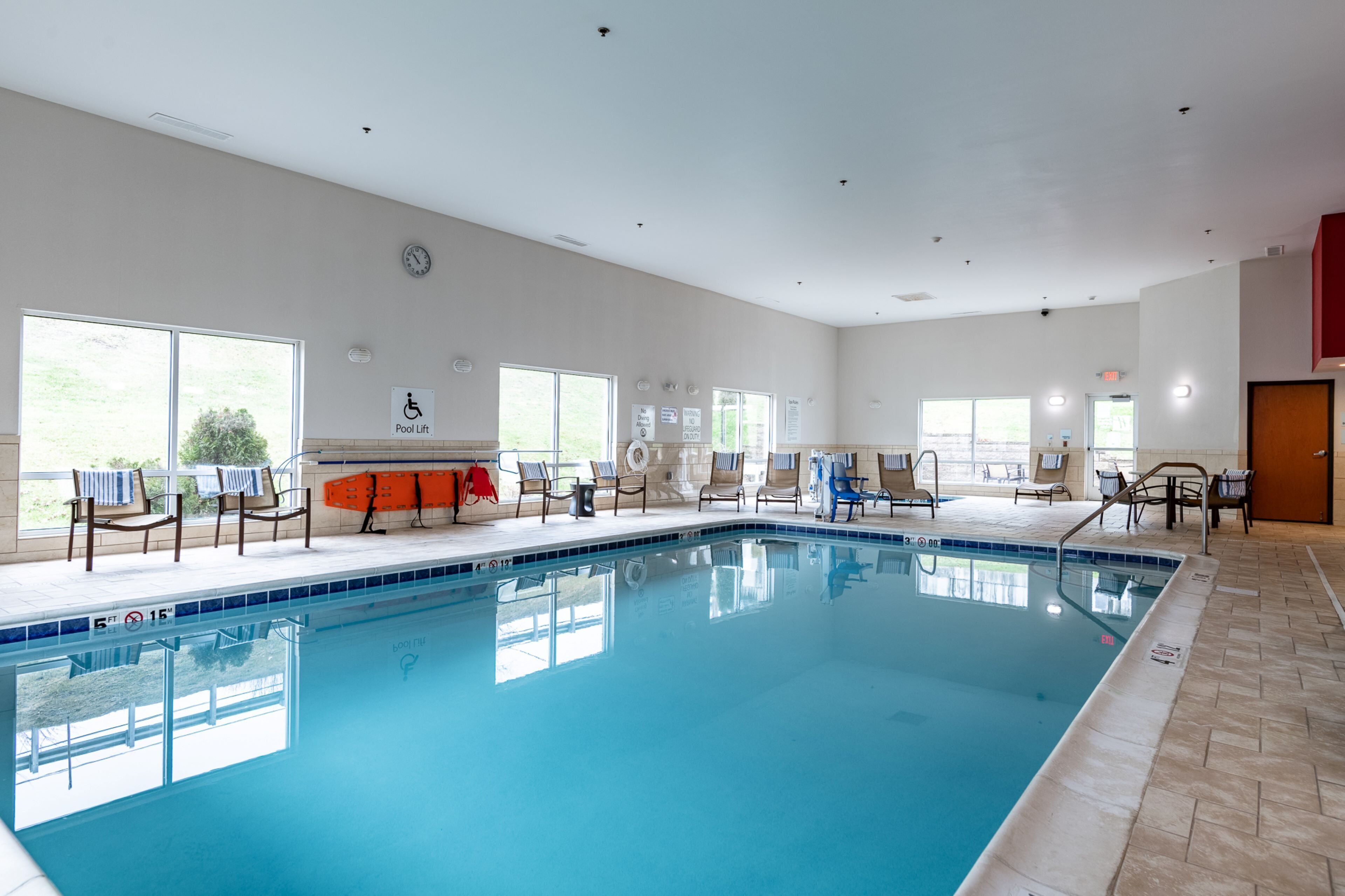 An indoor swimming pool with a lifeguard chair, lounge chairs, and a pool lift sign.
