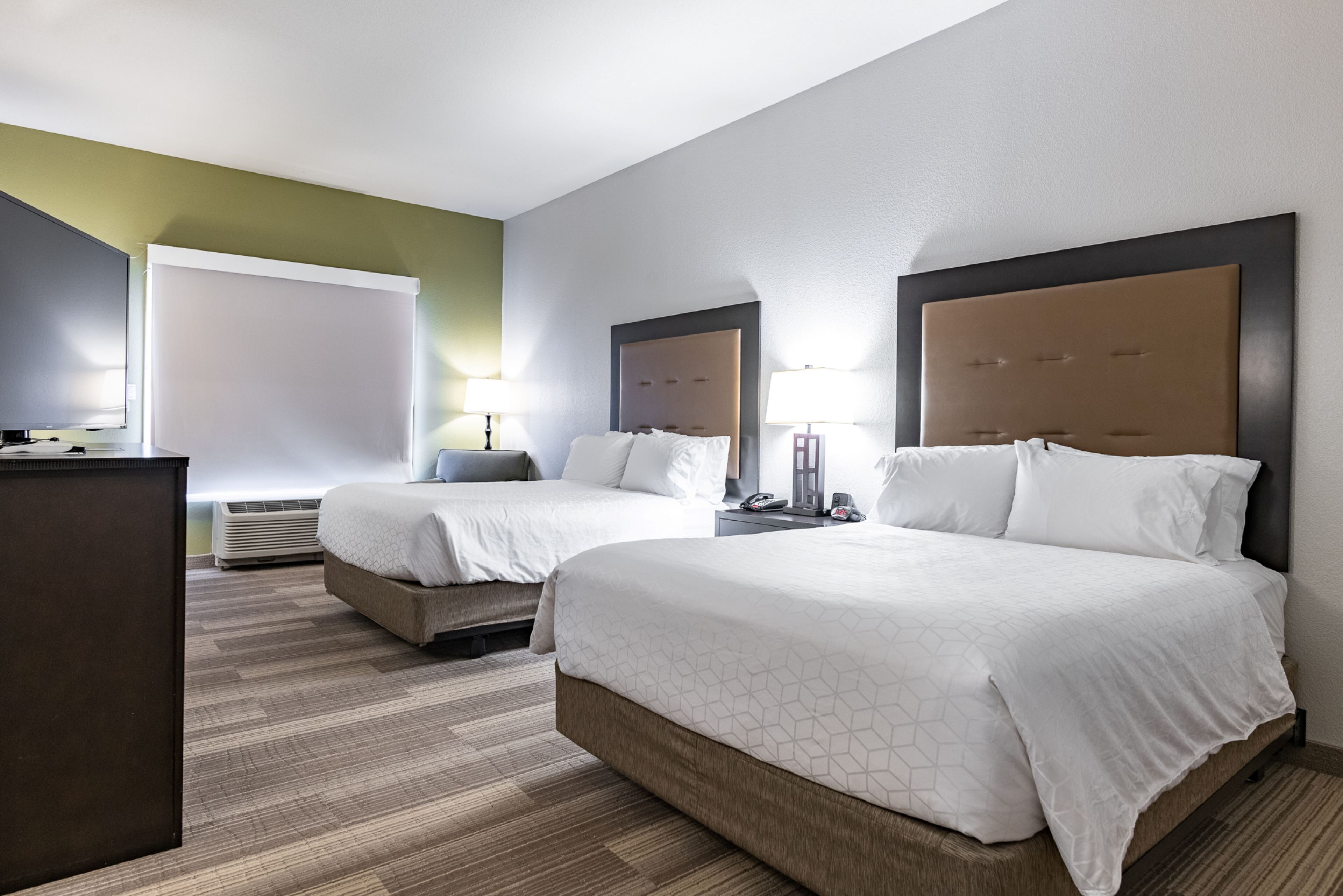 A hotel room with two beds, a desk, a chair, and a large window.
