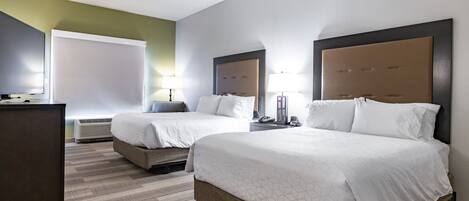 A hotel room with two beds, a desk, a chair, and a large window.