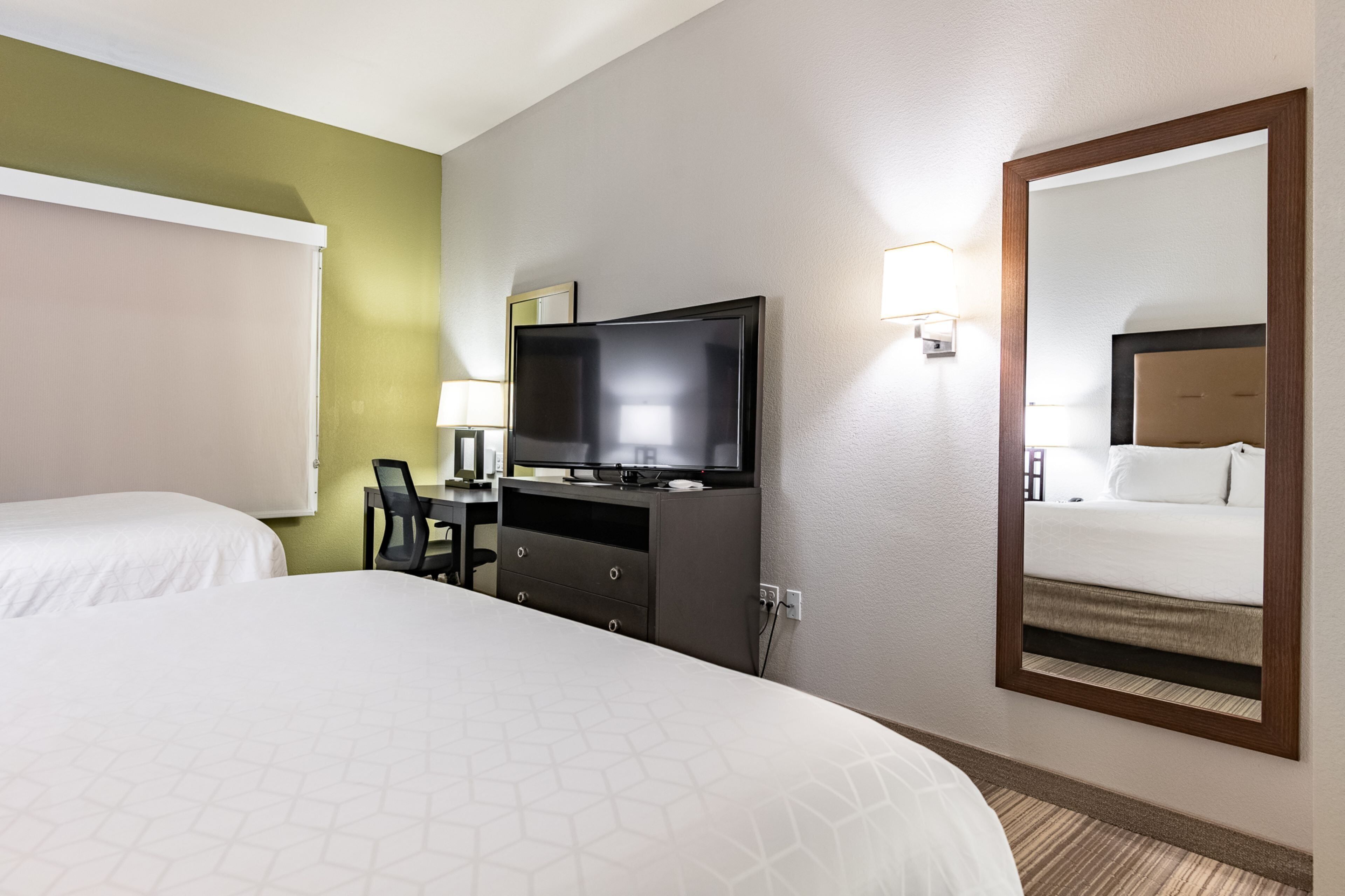 A hotel room with a bed, a desk with a chair, a television, and a large mirror.
