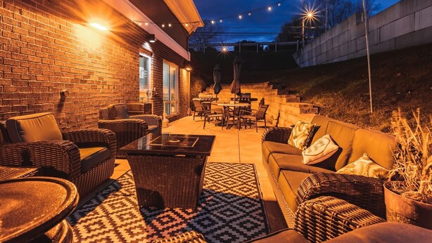 Un patio al aire libre con mobiliario de mimbre, una mesa con cubierta de vidrio y luces colgantes.