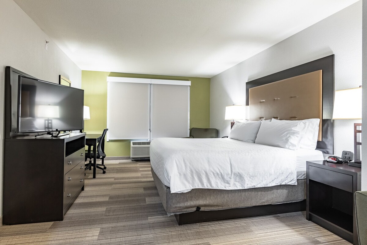 Una habitación de hotel moderna con una cama grande, un escritorio, un televisor y una ventana con persianas.