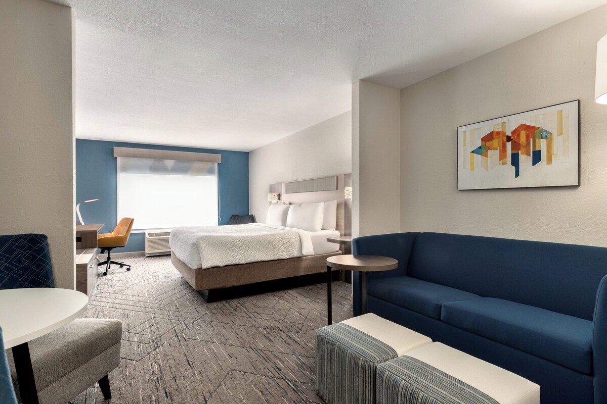 Habitación de hotel con cama, un sofá azul, una mesita, una silla y un cuadro en la pared.