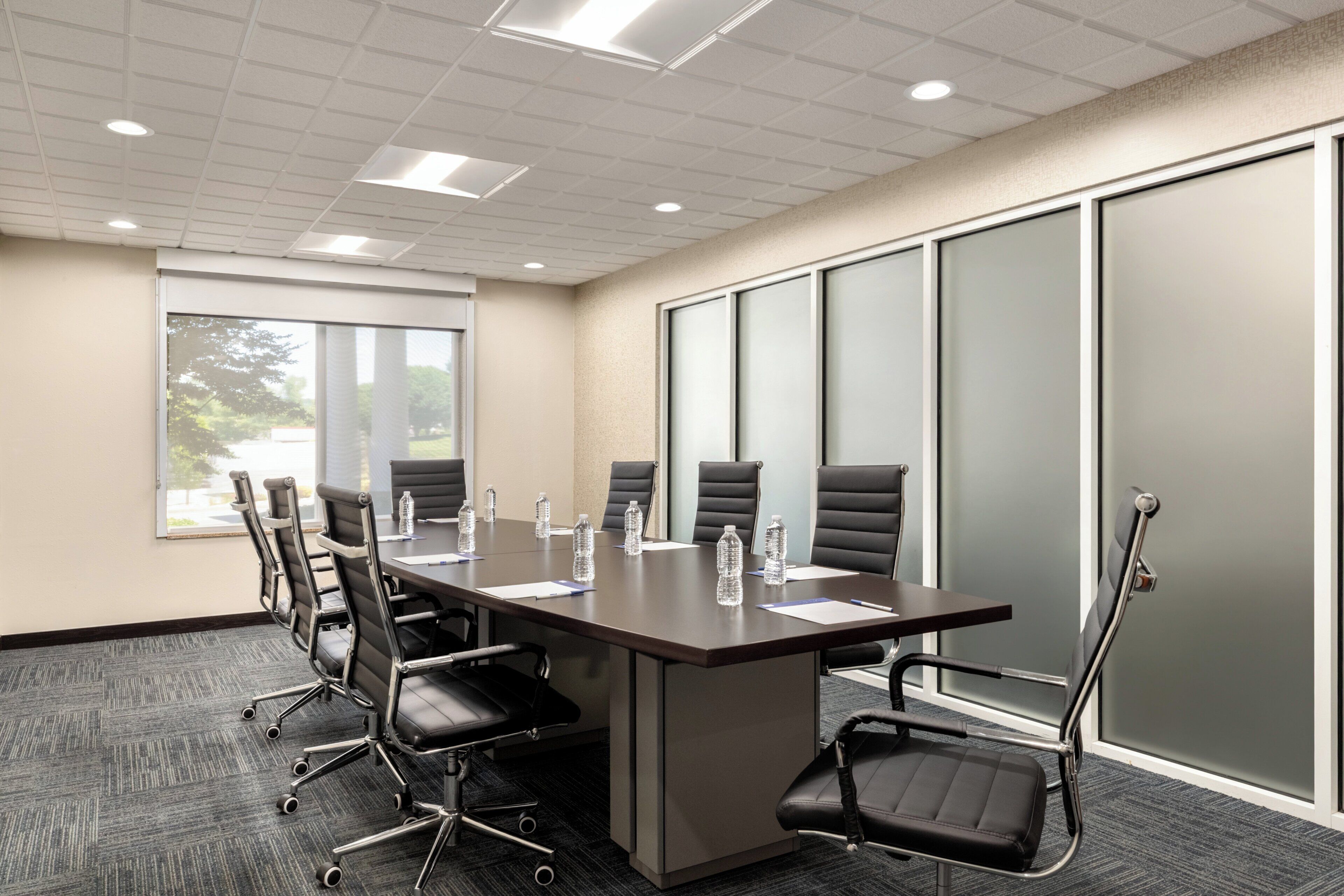 A conference room with a long table, chairs, water bottles, and a view through a window.
