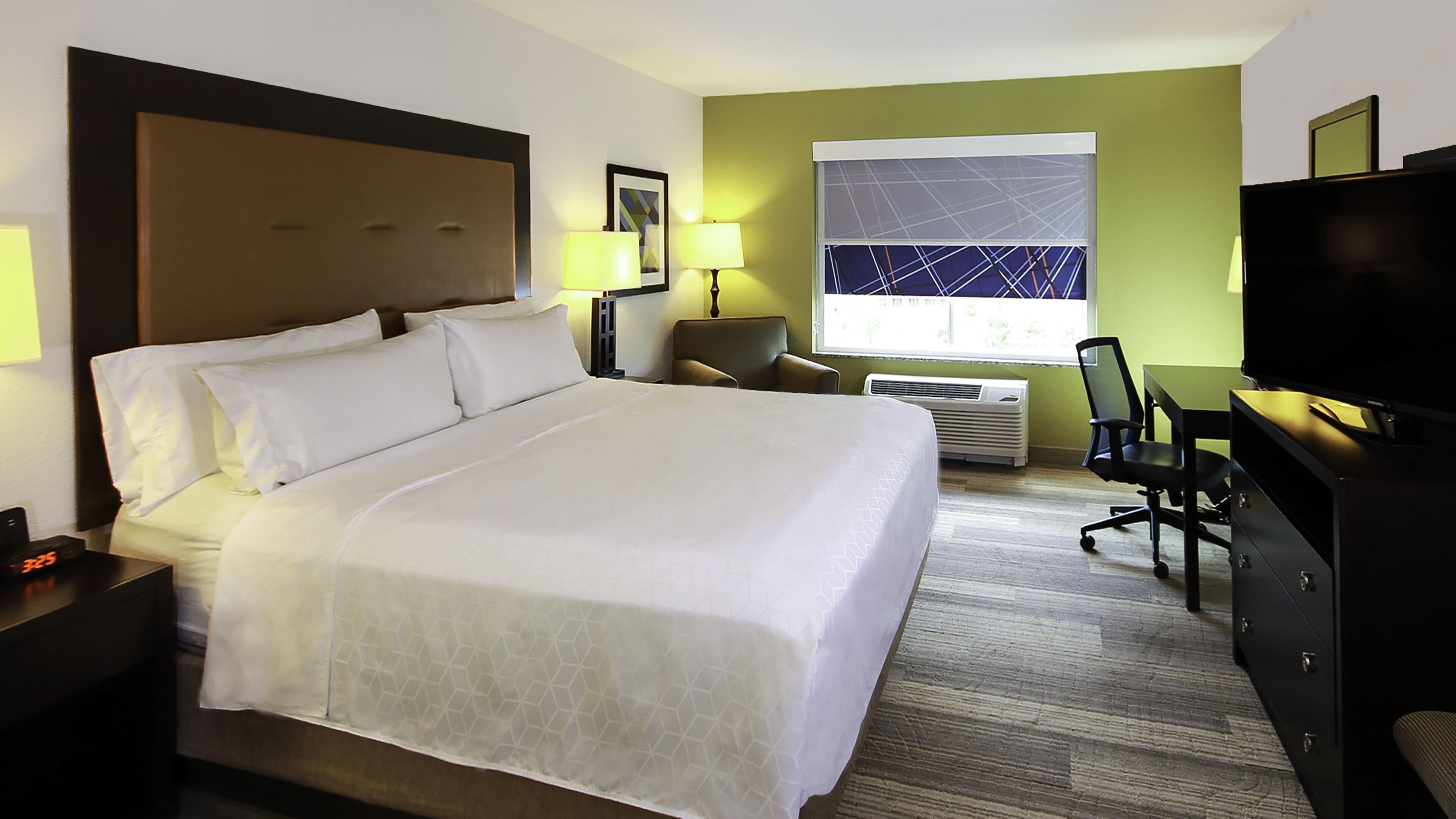 A hotel room with a large bed, a desk, a chair, a television, and a window with a view.