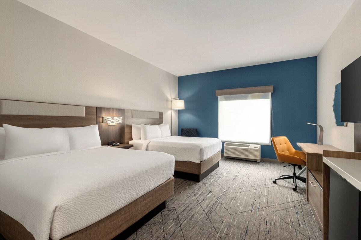 Habitación de hotel con dos camas, un escritorio, una silla, un televisor y una ventana con cortinas.