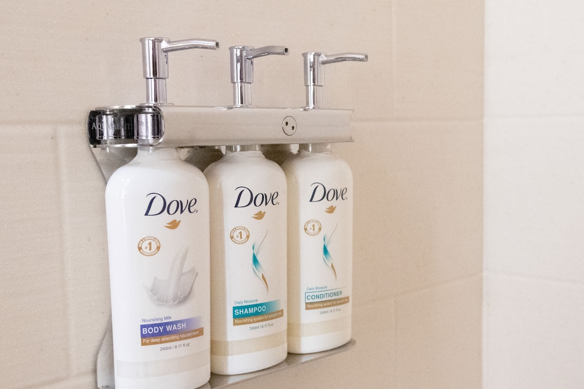 Three Dove personal care products mounted on a wall-mounted dispenser.