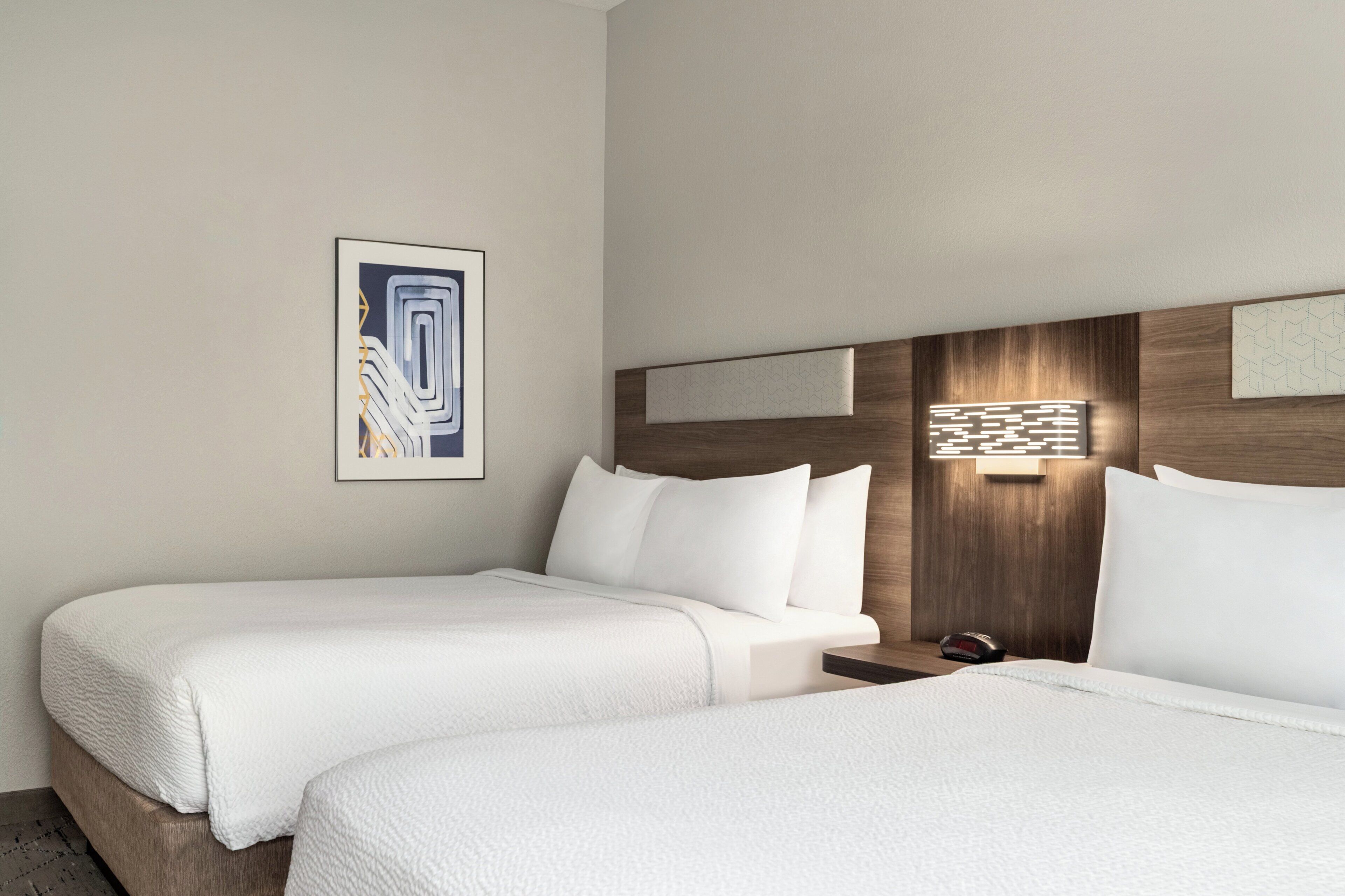 Een hotelkamer met twee bedden, een nachtkastje, een wandlamp en een ingelijste foto.