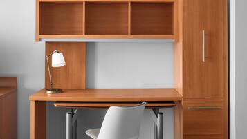 A wooden desk with a lamp, a chair, and a cabinet with drawers.