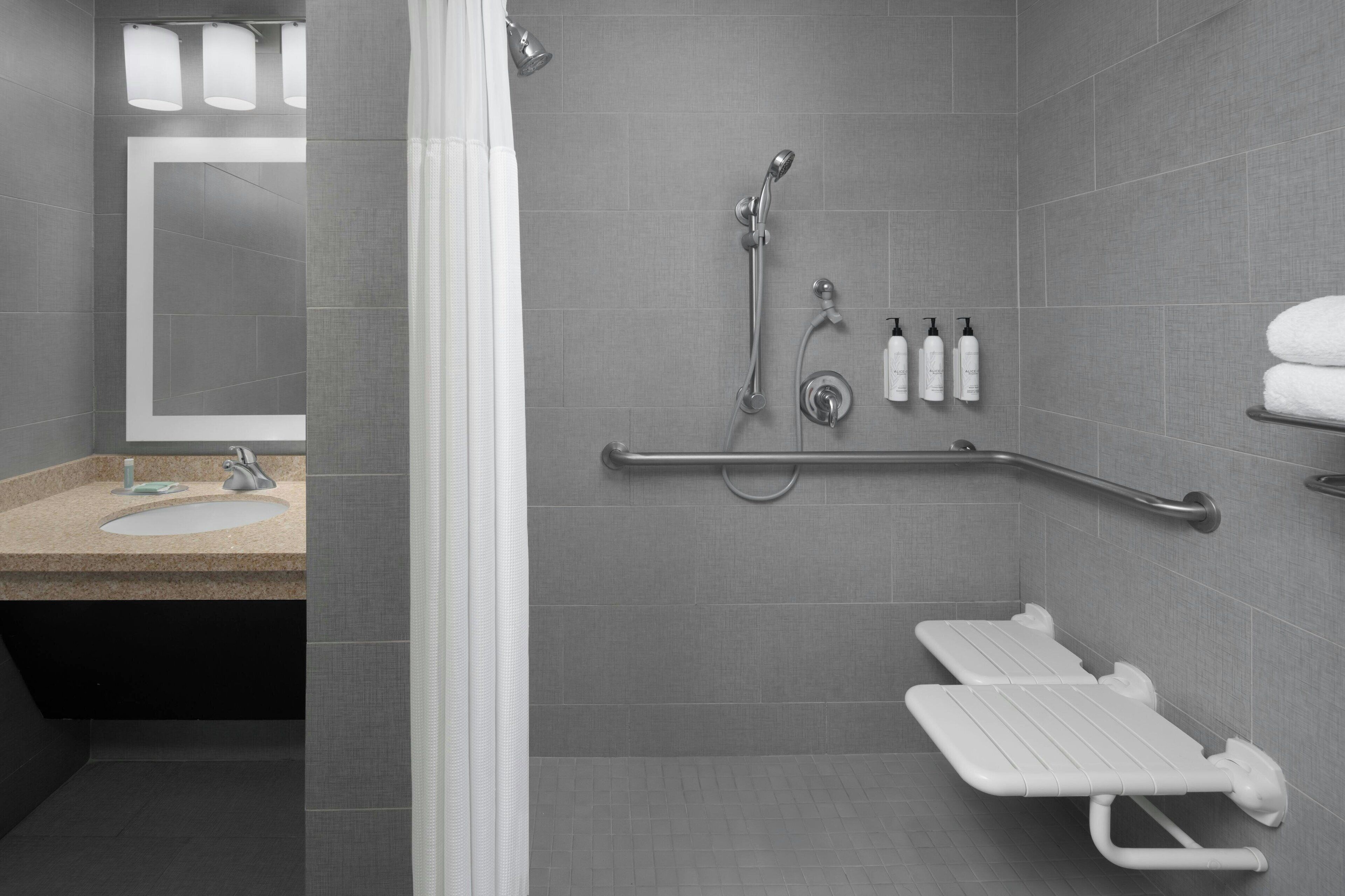 Un baño moderno con ducha, barras de apoyo, un banco y un lavabo.