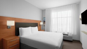 Una habitación de hotel moderna con una cama grande, cabecero de madera, lámparas de noche, un televisor de pantalla plana y una ventana con cortinas translúcidas.