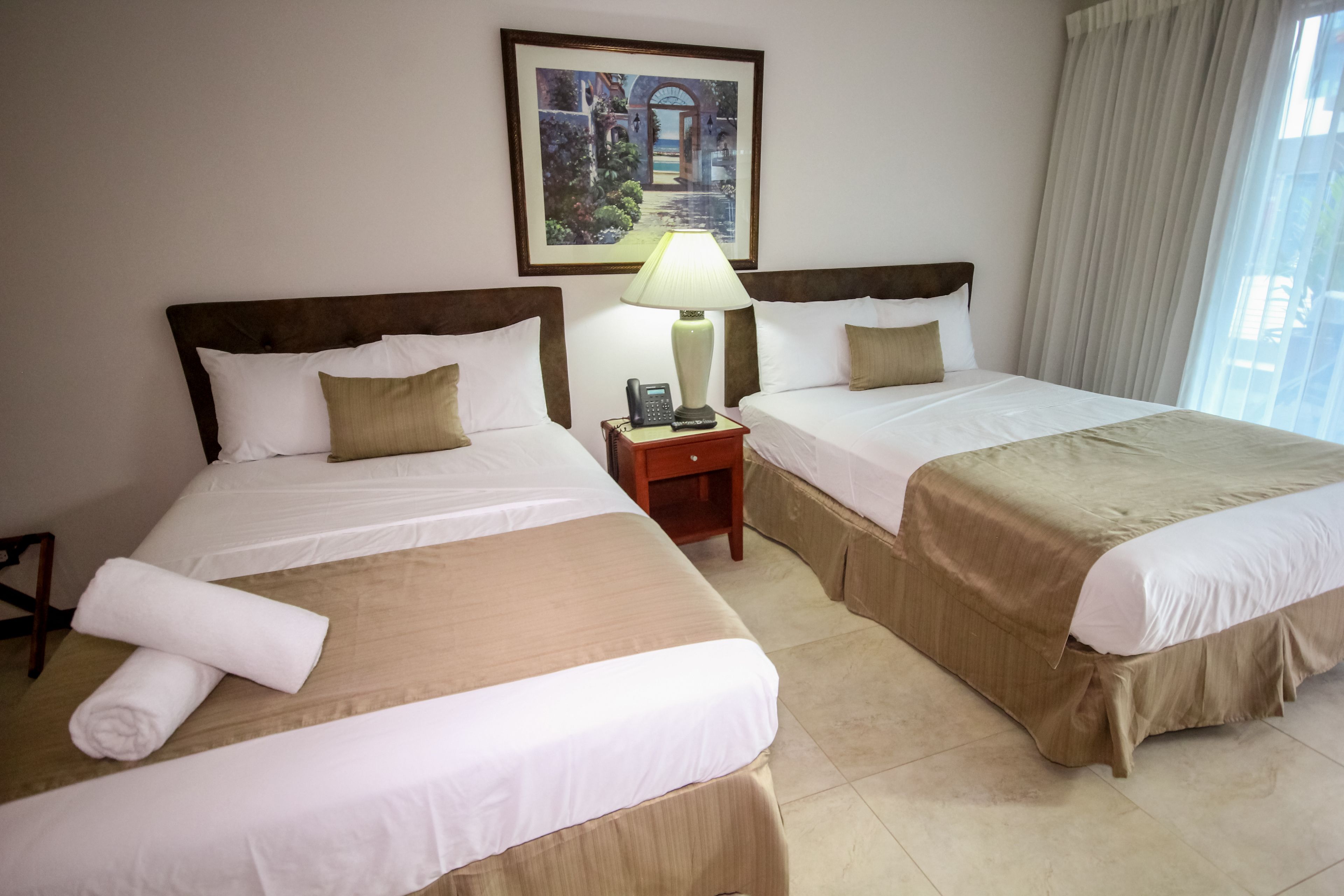 A hotel room with two beds, a nightstand with a lamp, and a painting on the wall.