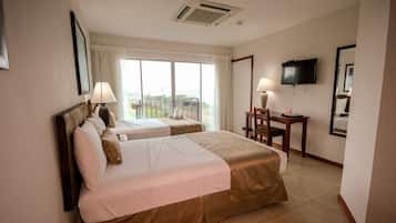 Quarto de hotel com duas camas, uma escrivaninha, uma cadeira, uma televisão e uma janela grande com cortinas.