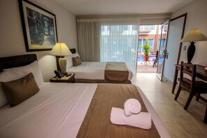 A hotel room with two beds, a desk, a chair, a lamp, and a view of the outdoor area. - Hotel Tramonto (Jacó)
