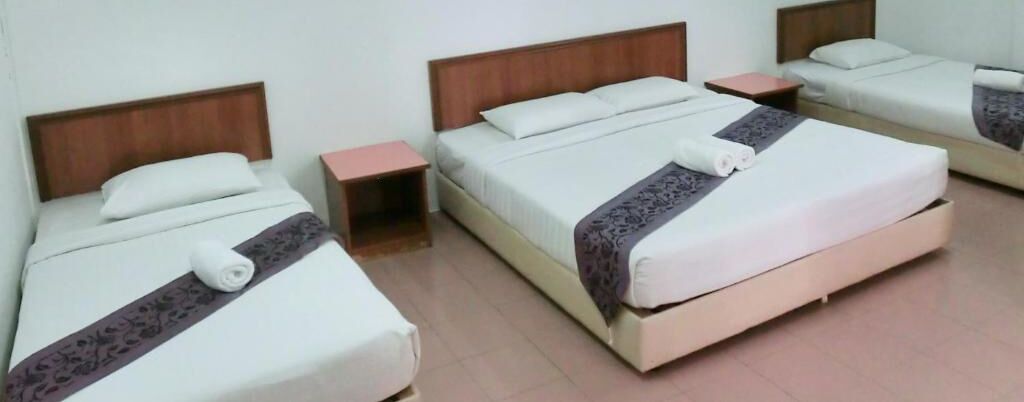 A hotel room with two beds, each with a wooden headboard, a bedside table, and a white bedspread.