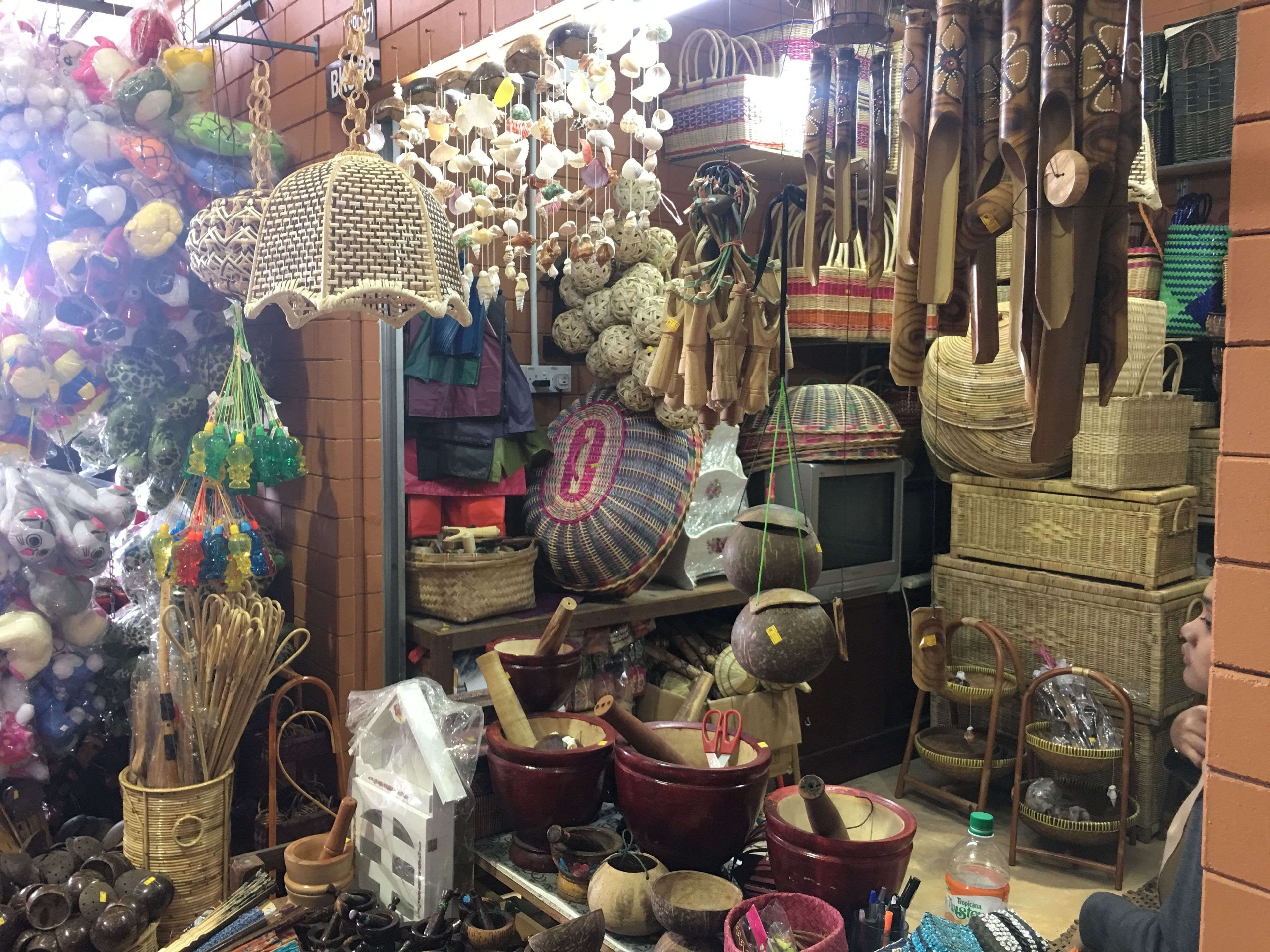 A cluttered market stall with various items including woven baskets, pottery, and hanging decorations.