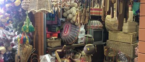 A cluttered market stall with various items including woven baskets, pottery, and hanging decorations.