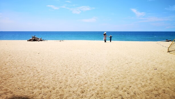 Una extensa playa de arena, cielo azul despejado y mar tranquilo.