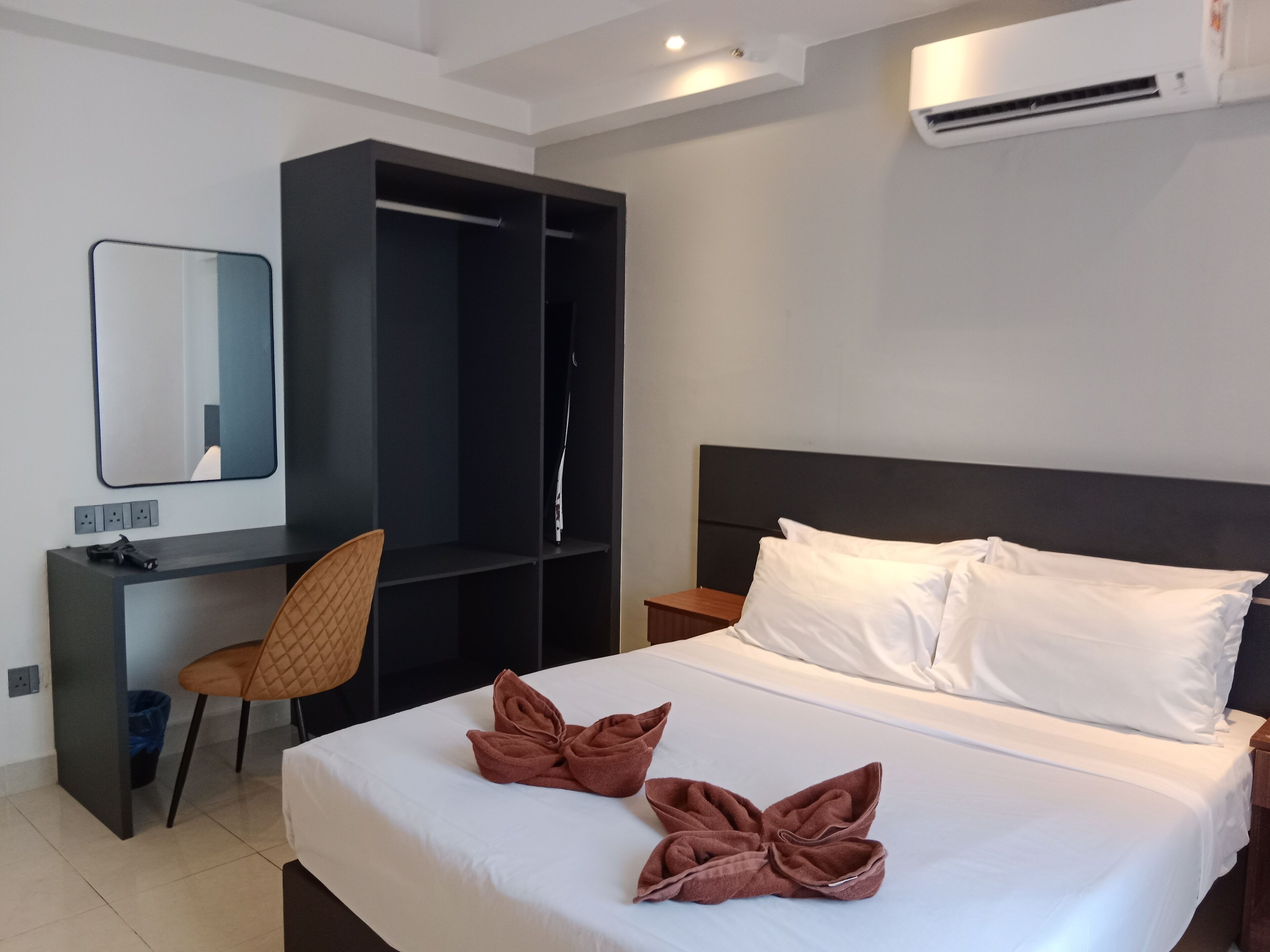 Habitación de hotel con cama, escritorio, silla, armario y aire acondicionado.