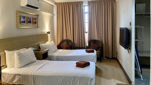 Habitación de hotel con dos camas, televisión, ventana con cortinas y aire acondicionado instalado en la pared.