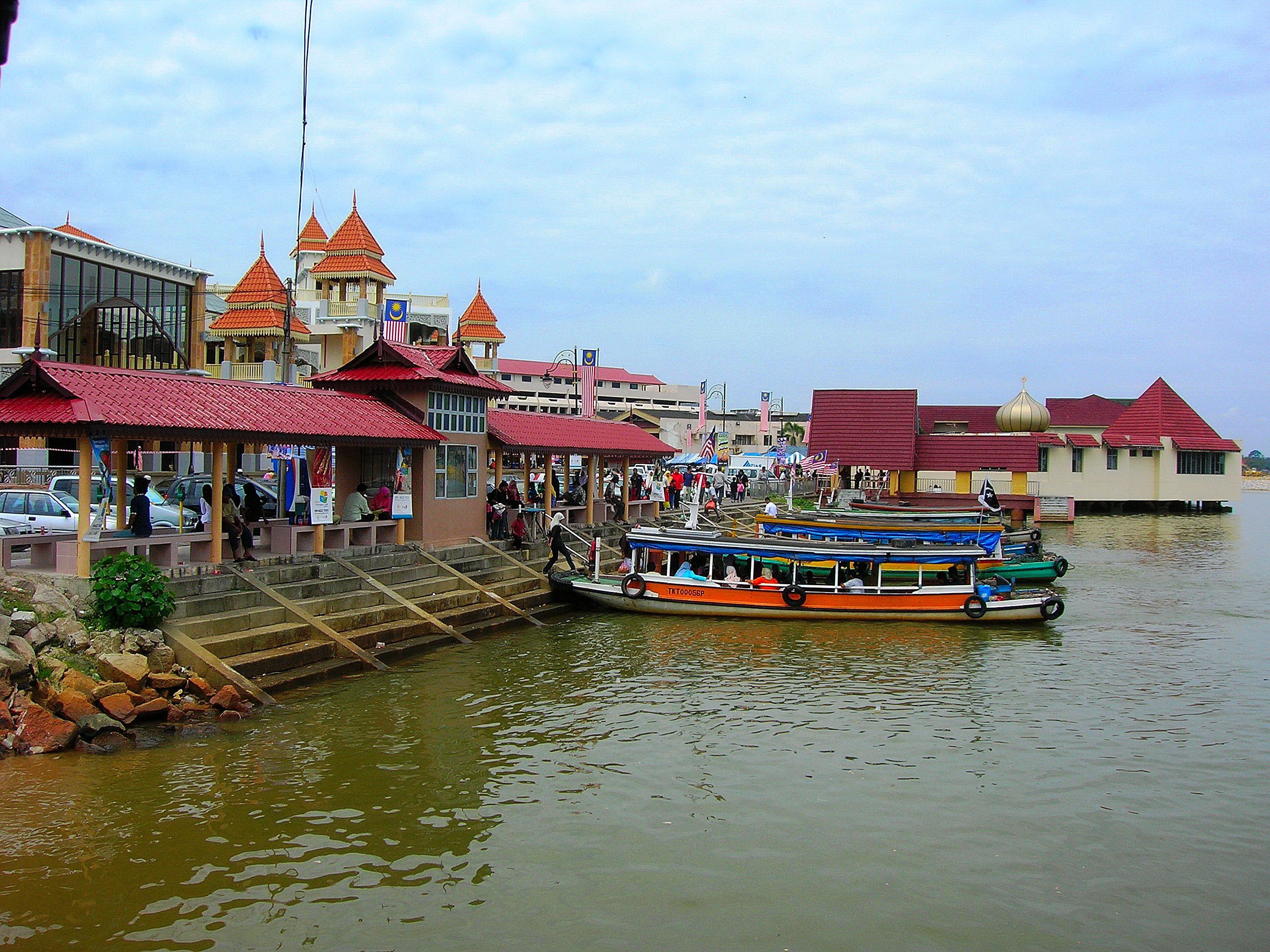 Una zona junto al río con barcos, escaleras que bajan al agua y edificios con tejados rojos.