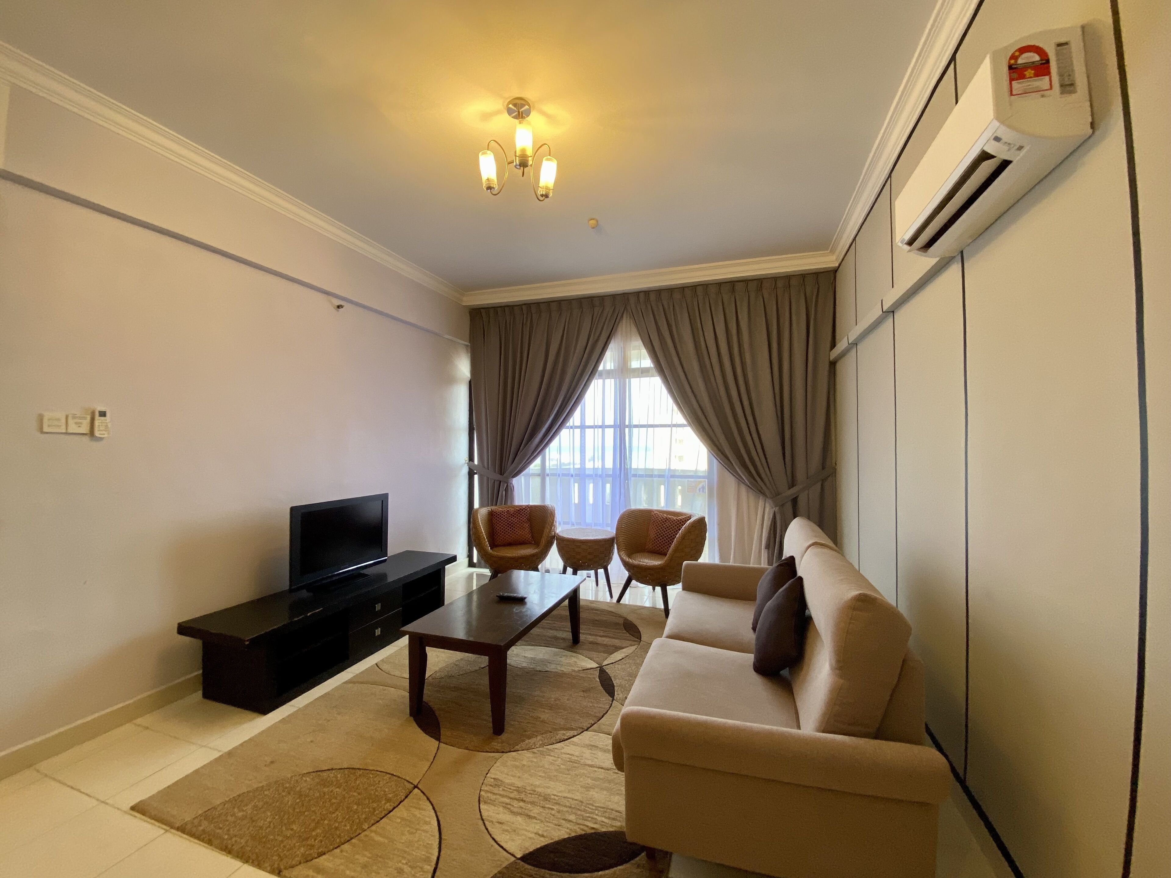 A living room with a sofa, two armchairs, a coffee table, a flat-screen TV, and an air conditioning unit.