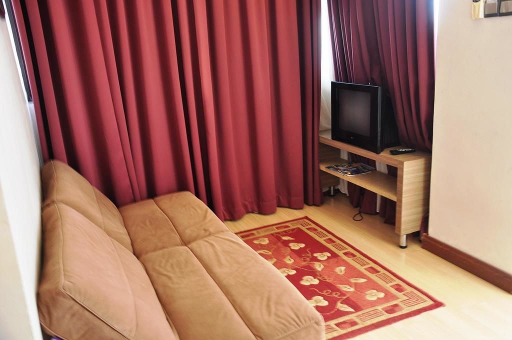 A living room with a beige sofa, a television on a wooden stand, and a red curtain.