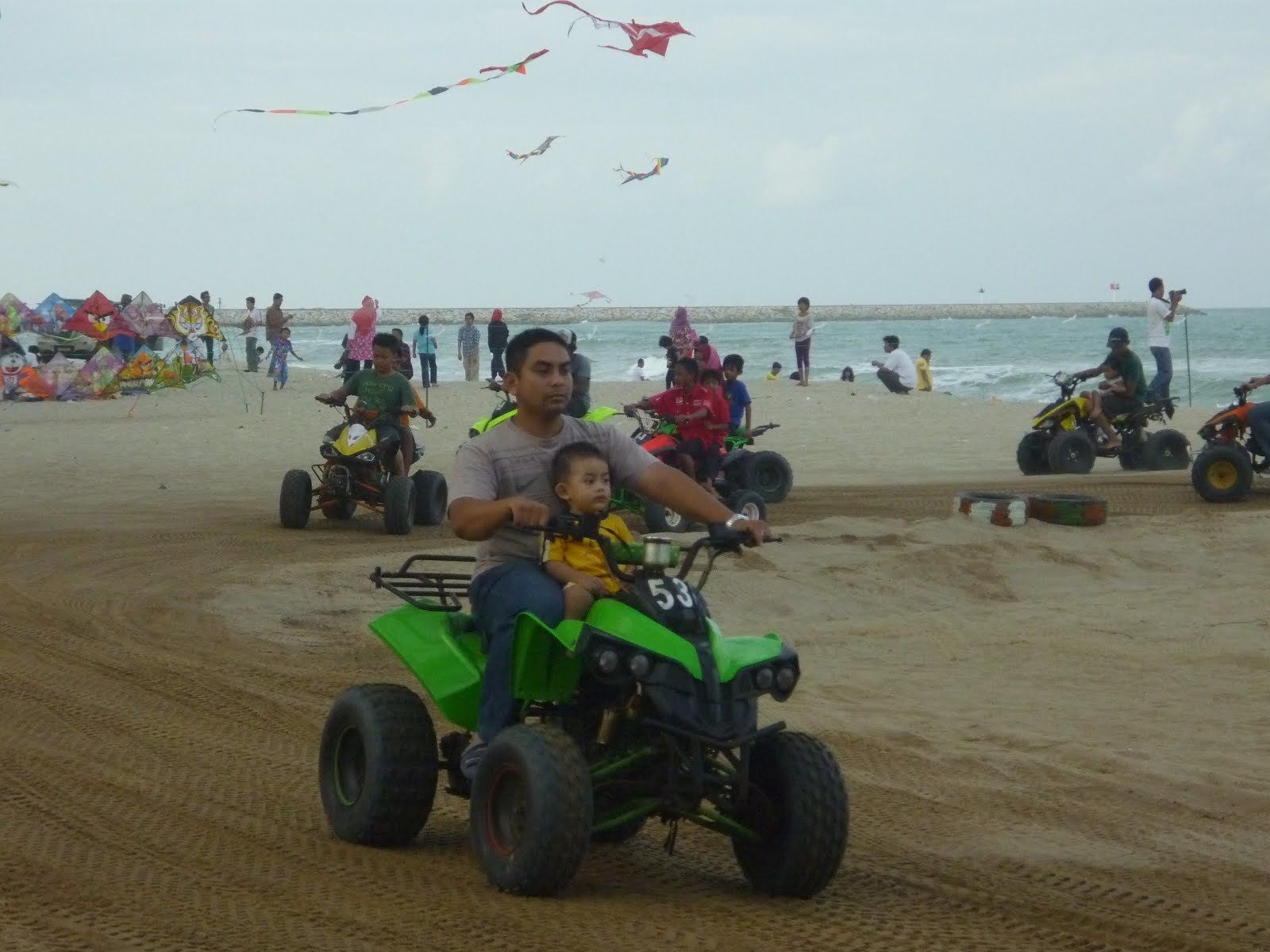 A sandy beach with people on quad bikes and children playing.