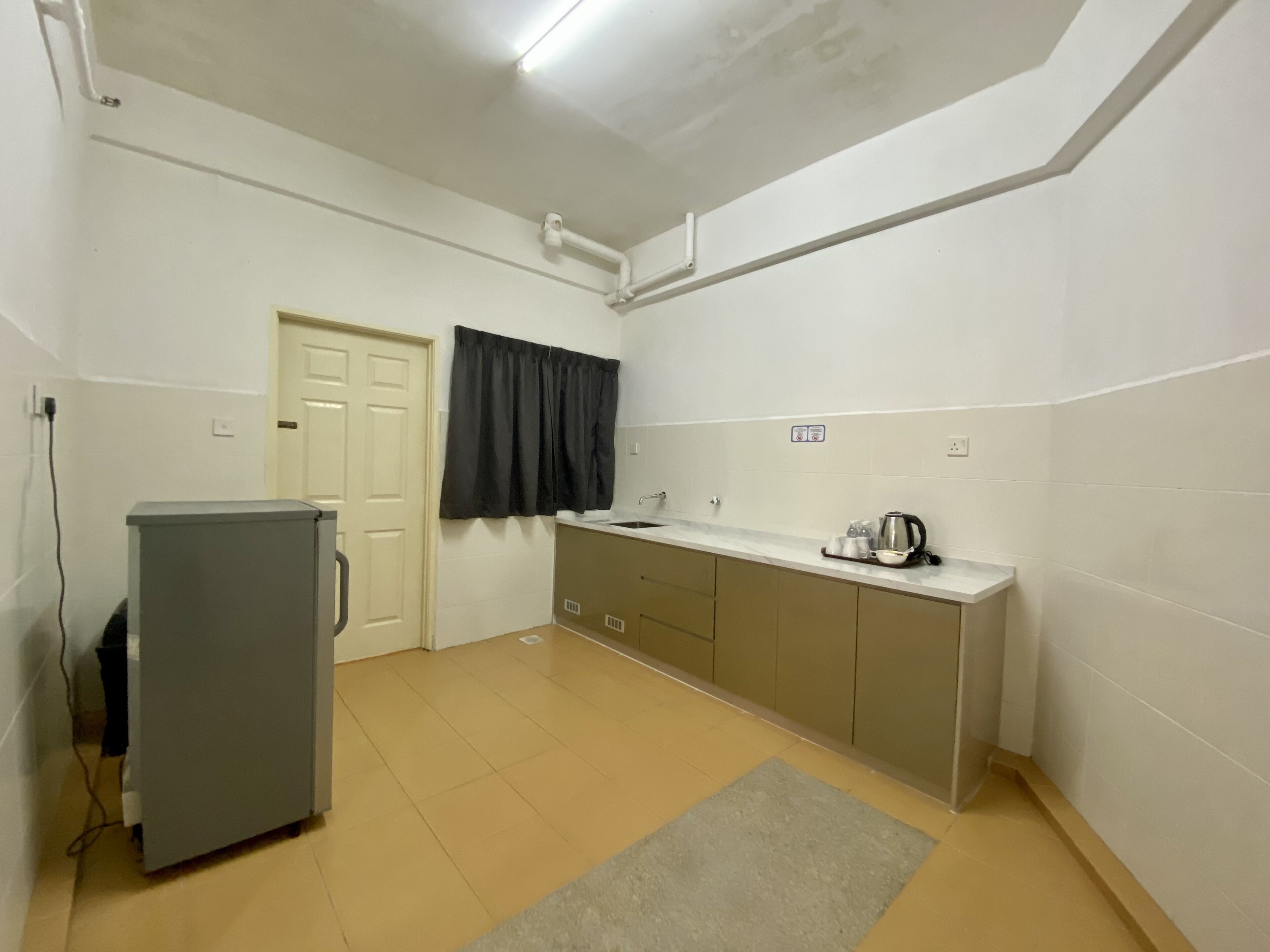 A compact kitchen with a refrigerator, a sink, and a kettle on the counter.