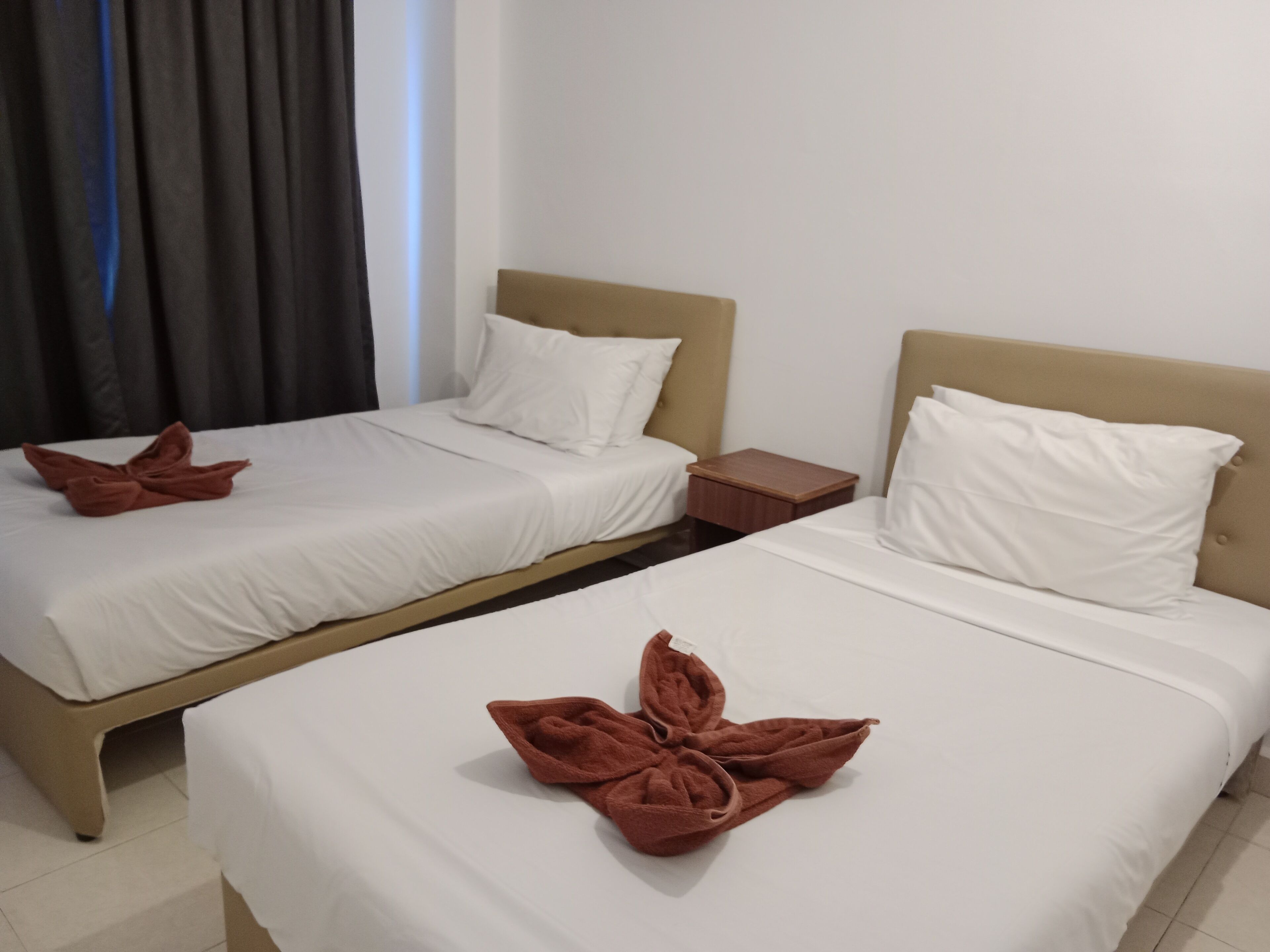 Two twin beds with white linens and brown towels folded on them.